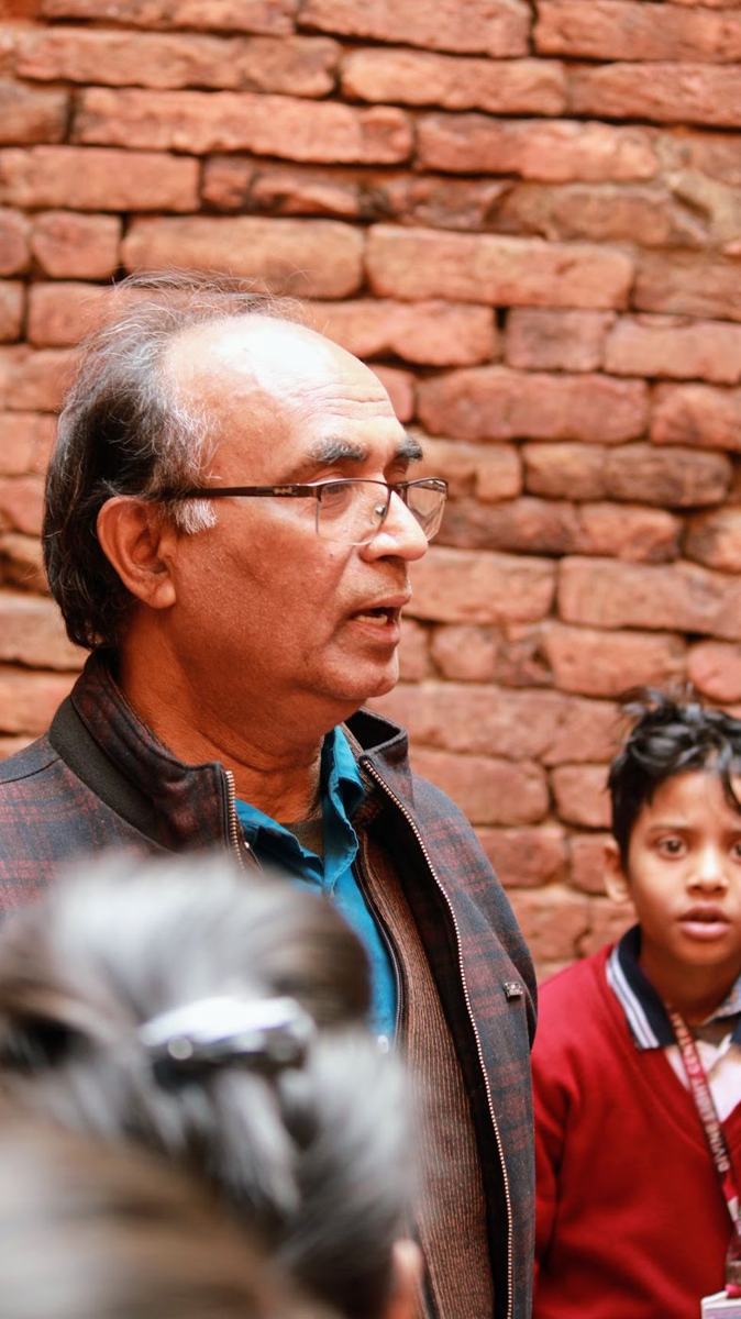 The director explaining history to students beside an ancient brick wall